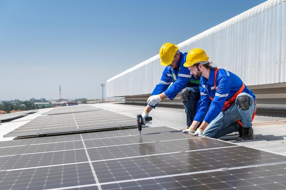 Workers installing large commercial solar panels on a factory rooftop in Thailand.
